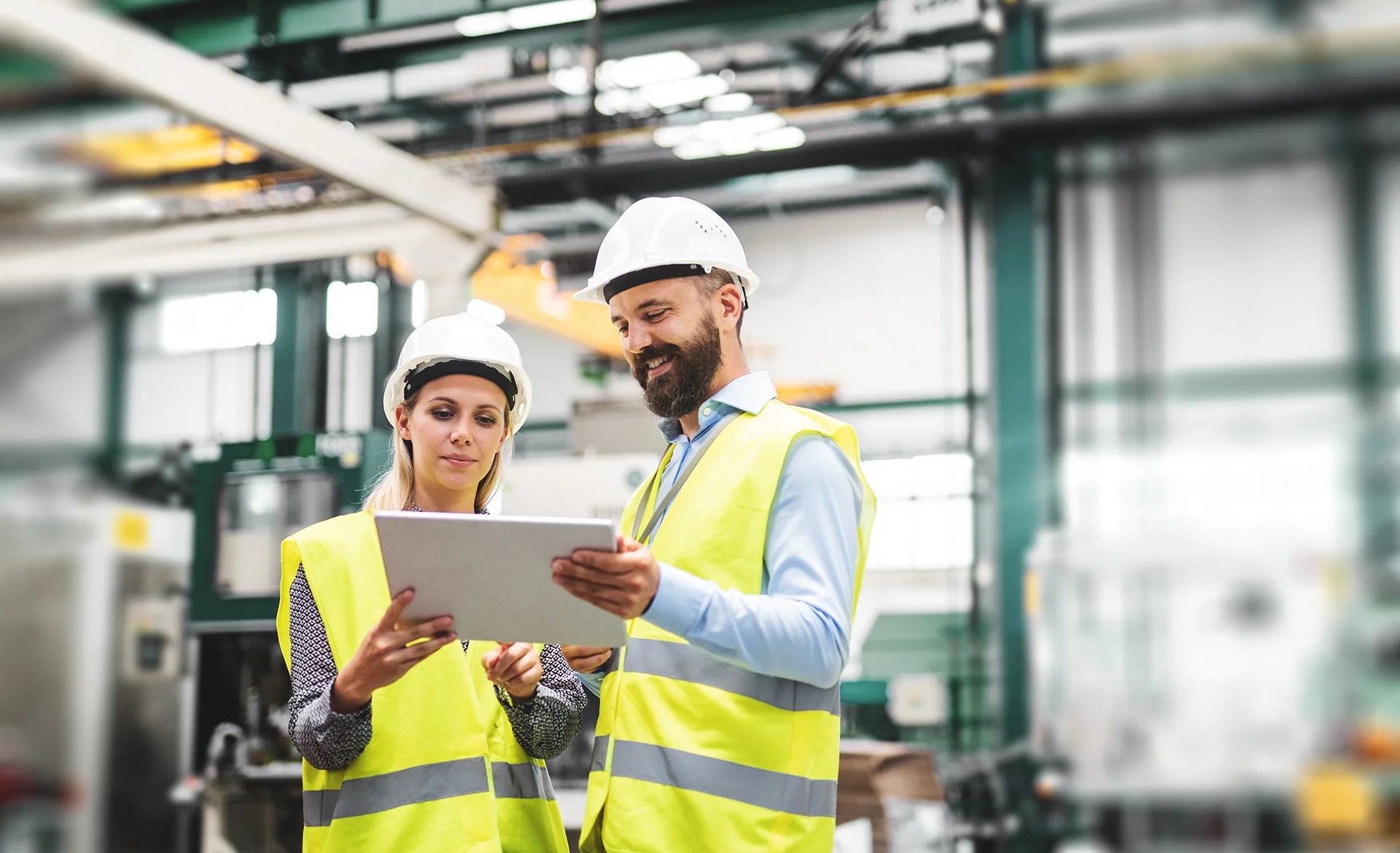 Un homme et une femme ingénieurs avec une tablette dans une usine, en train de discuter.